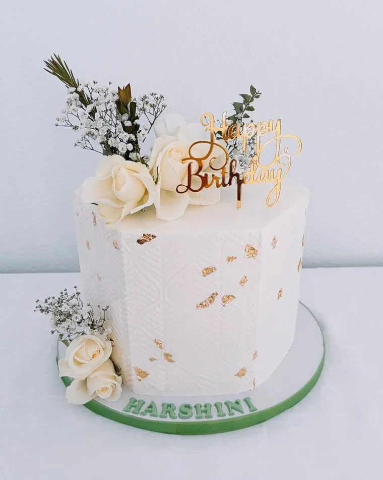 White textured cake with gold leaf, fresh roses and a gold Happy Birthday topper