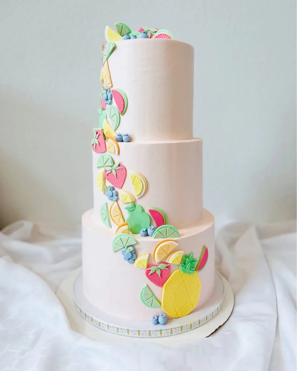 Three-tier blush buttercream cake with a cascade of sugar fruit