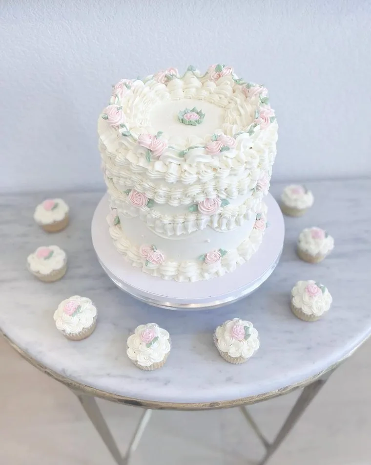 Vintage piped white cake with pink rosettes and matching cupcakes on a marble table