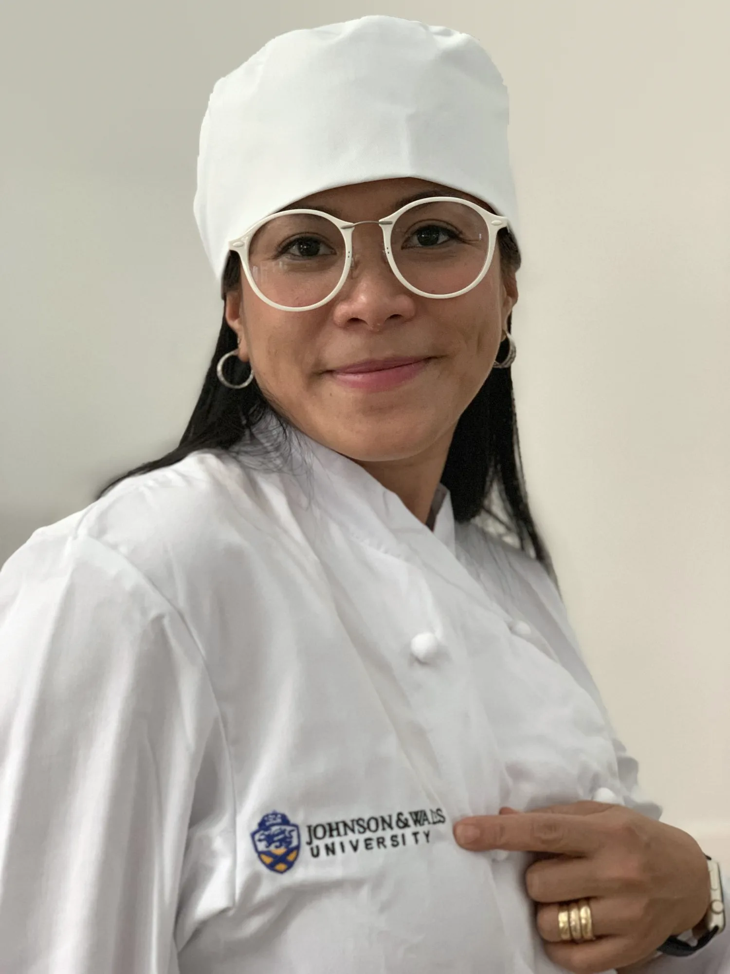 Ellah in her chef's whites and hat, pointing to the Johnson & Wales University logo on her jacket